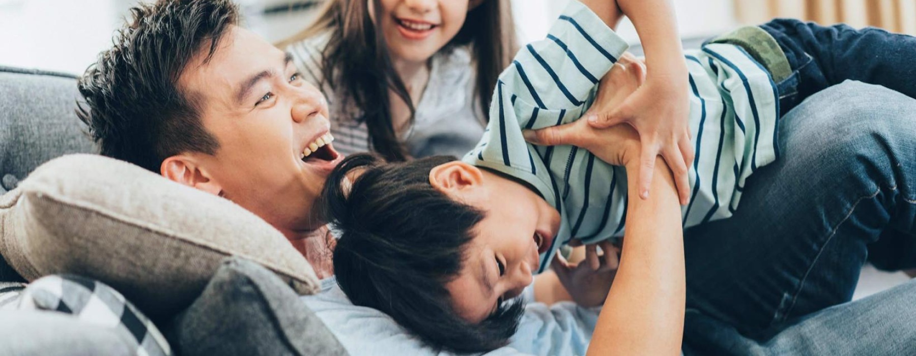 father plays on a couch with his young children