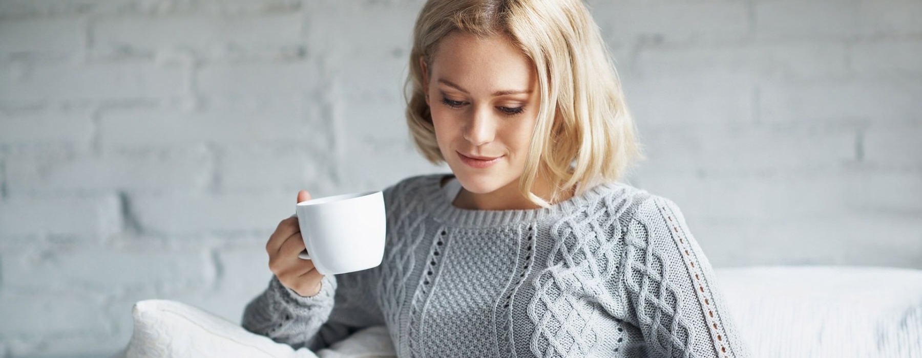 woman sitting on a couch next to a large window with a cup of tea in her hands